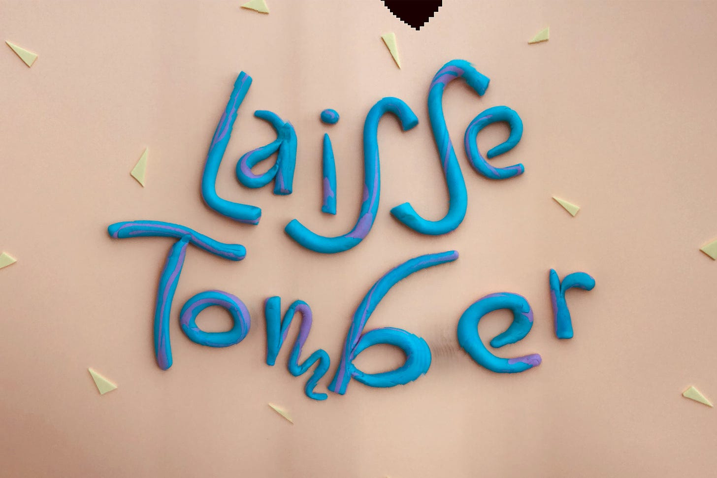 Clay letters that say "Laisse Tomber" or "let it go" on a paper background surrounded by foam triangles