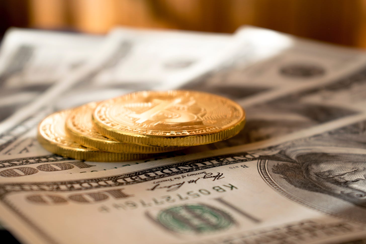 Three gold Bitcoins on four USD$100 bills.