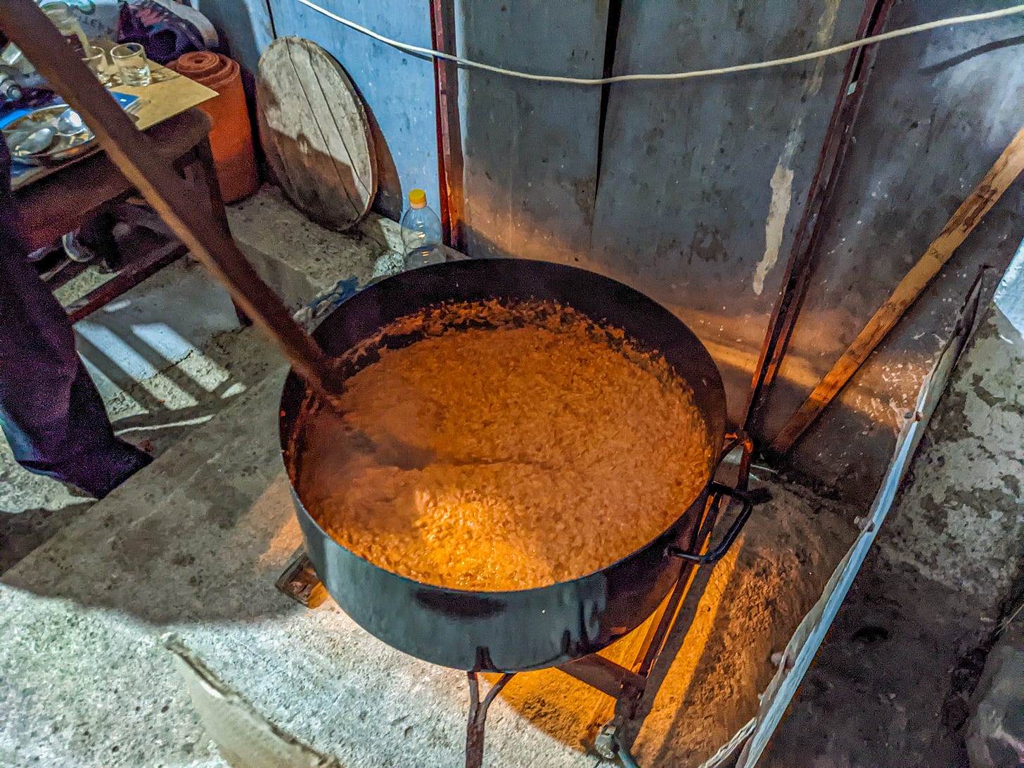 A black kettle filled with orange-colored ajvar simmering over a fire. 