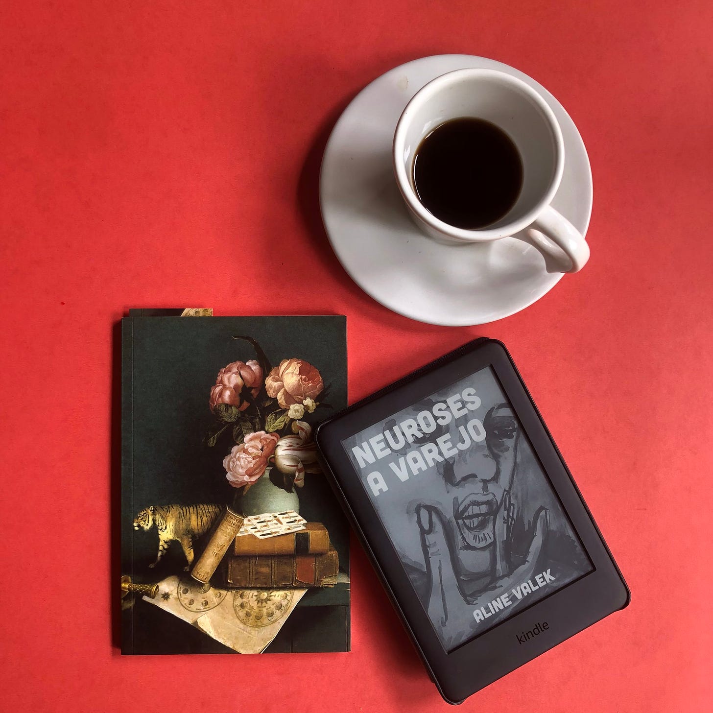 um kindle com a capa de neuroses a varejo ao lado de um caderno e uma xícara de café, sobre fundo vermelho