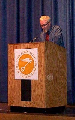 The author stands behind a podium marked "The Scholastic Art & Writing Awards," reading a speech on a stage with a blue curtain behind him.