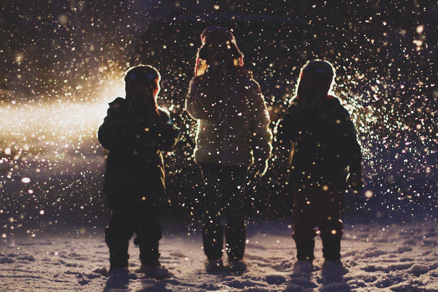 The silhouette of three children standing in the snow.