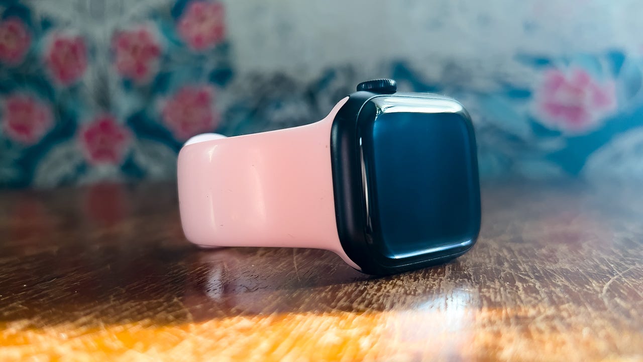 An Apple Watch Series 8 with a pink band in front of a floral background