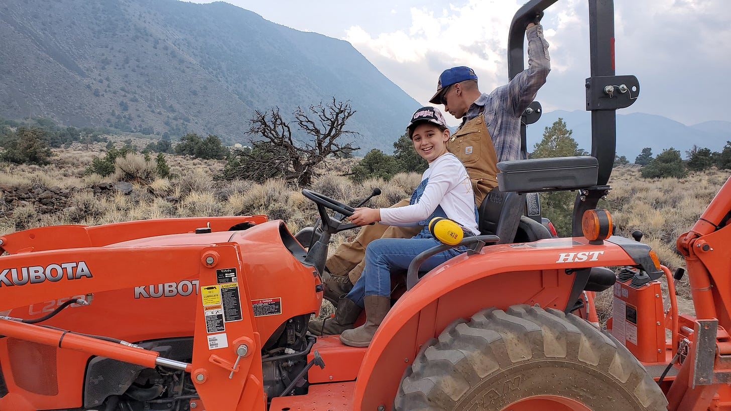C and Eric on a Kubota tractor. C is smiling at the camera while Eric looks down to the right.