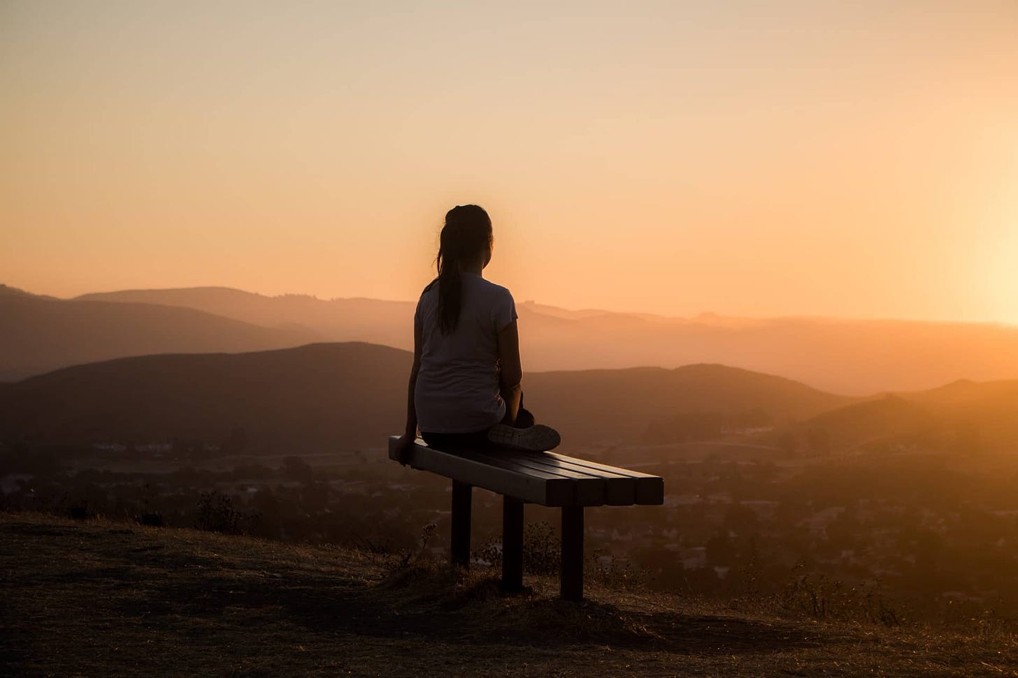 An image relating to creating a decision ritual. It's a woman sitting on a park bench overlooking a city during sunrise.