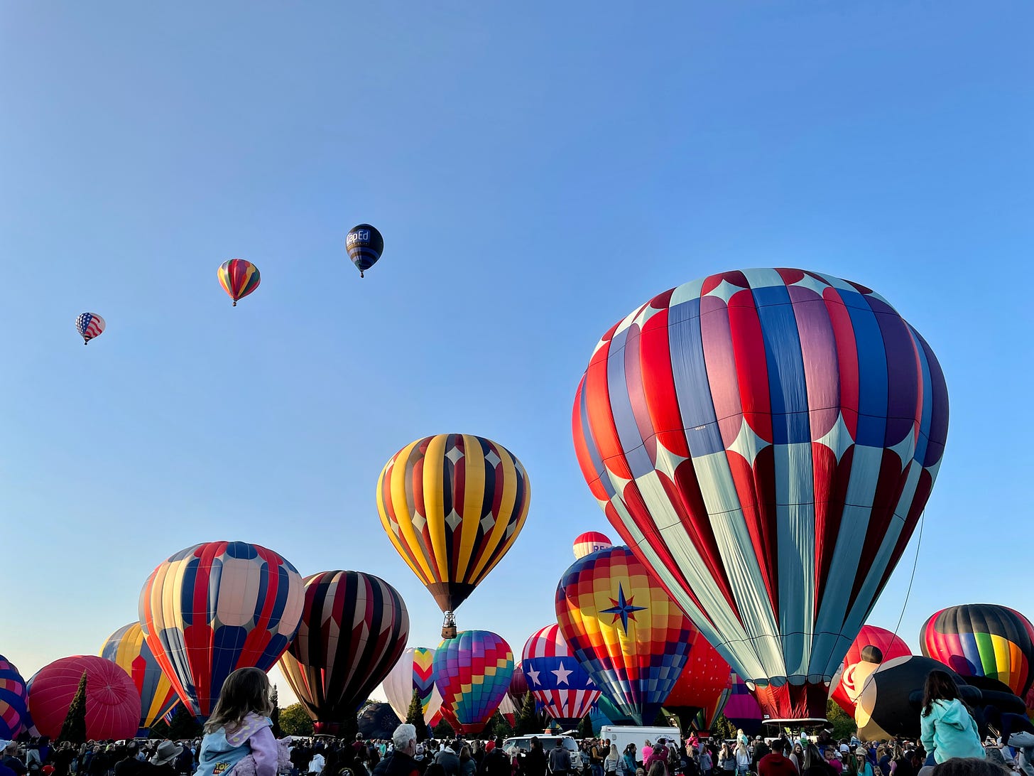 Brightly colors hot air balloons filling slowly, crowding the morning sky