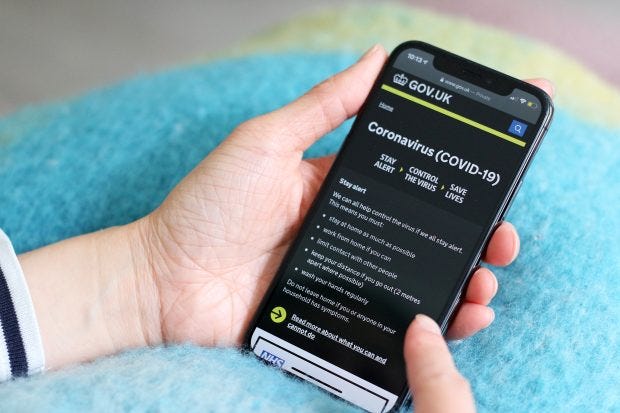 A person holding a mobile phone showing the GOV.UK coronavirus page reading: ‘Coronavirus (COVID-19)’ – stay alert, control the virus, save lives