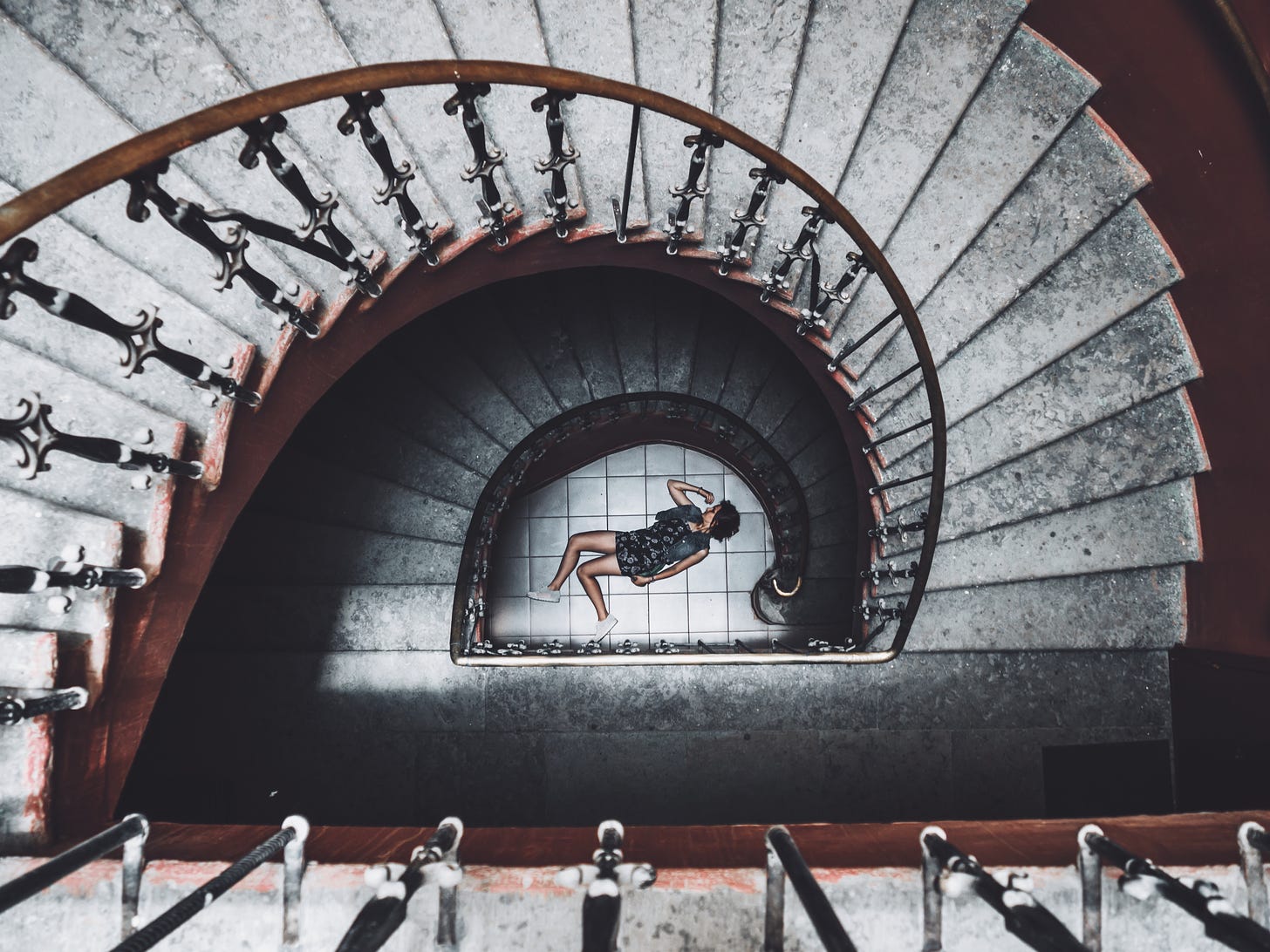 aerial view of a stone spiral staircase with a woman lying on the ground at the bottom of the stairs