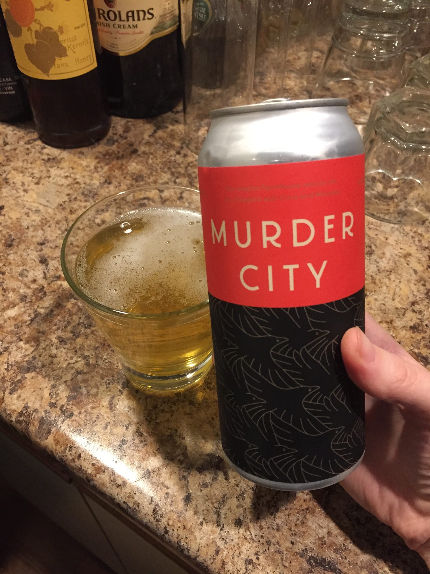 my hand holding a black and red can of beer, in front of a glass of pale beer. The top red half of the can reads 'MURDER CITY' and the black bottom half is patterned with stylized crows.