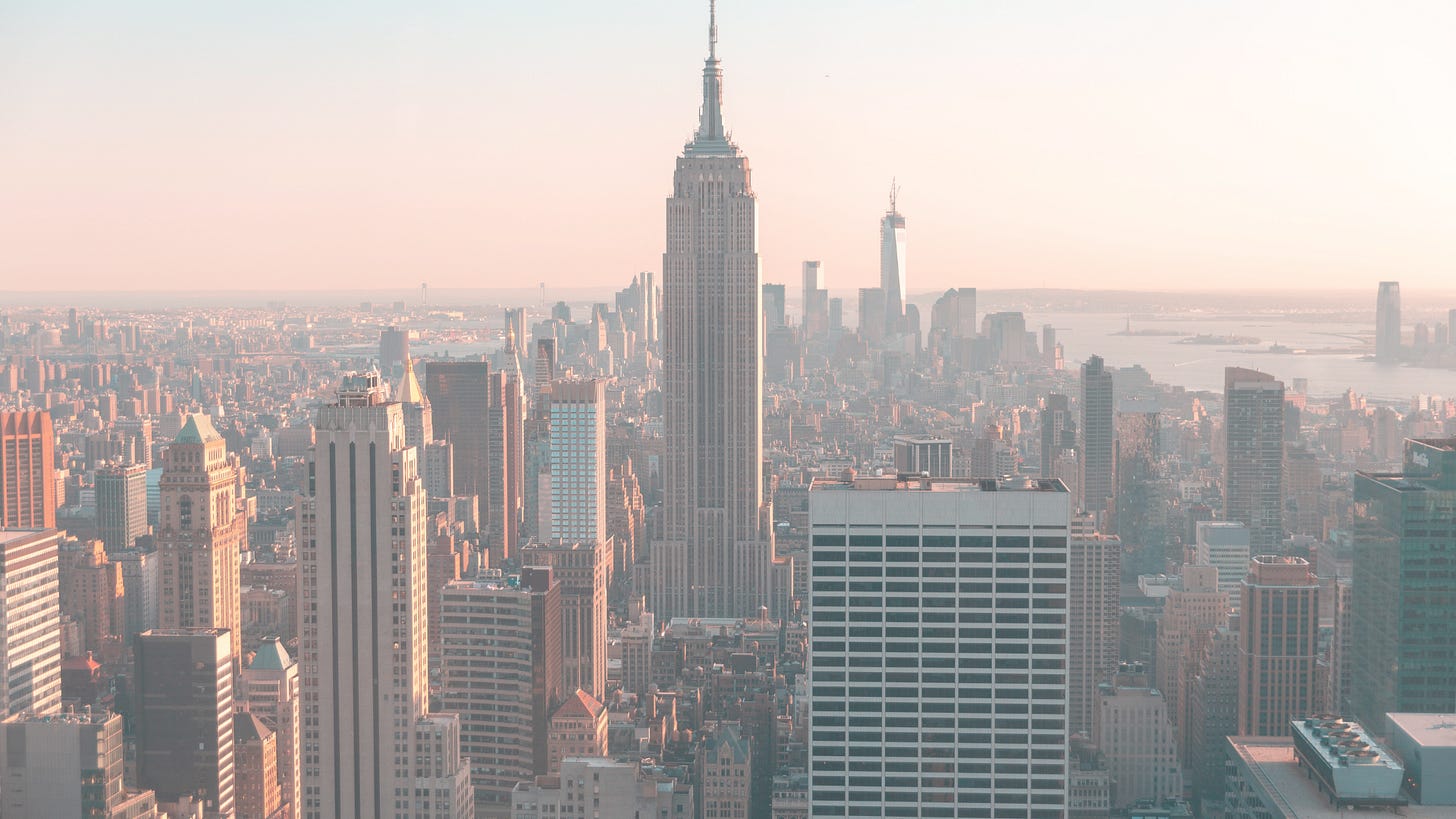 Manhattan downtown skyline with illuminated Empire State Building and skyscrapers at sunset.