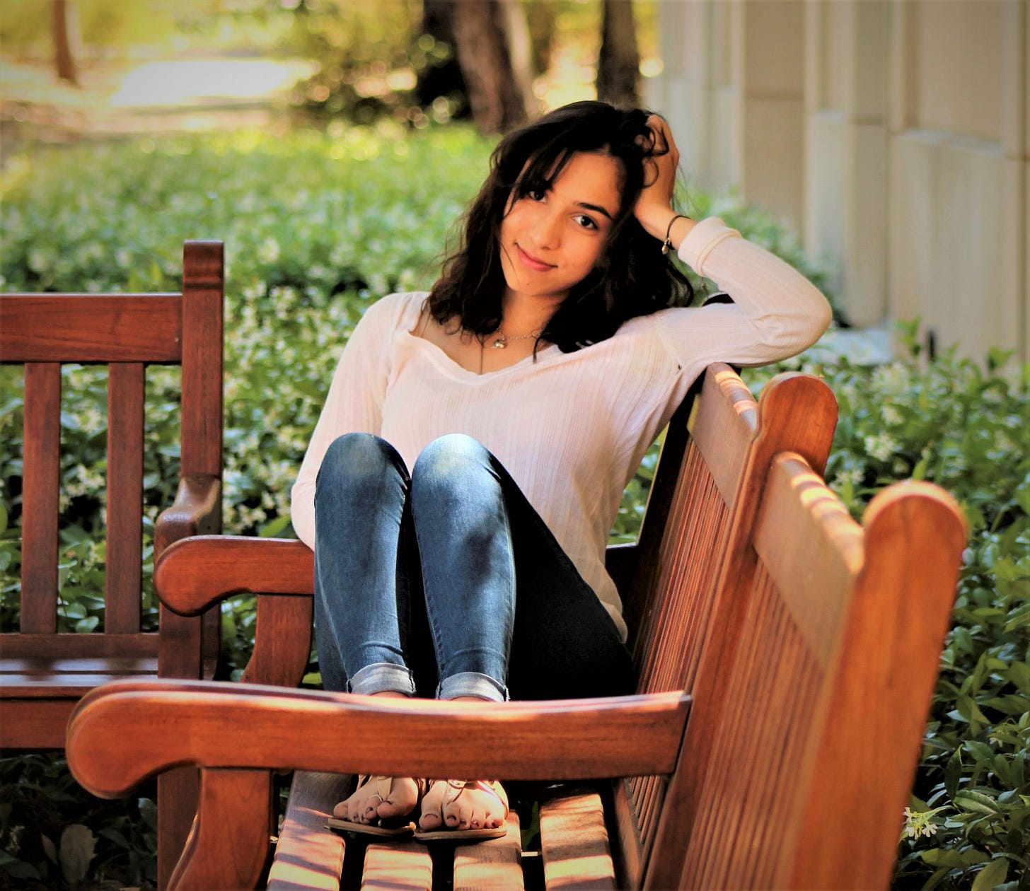 happy girl with dark hair wearing jeans sitting on wooden bench