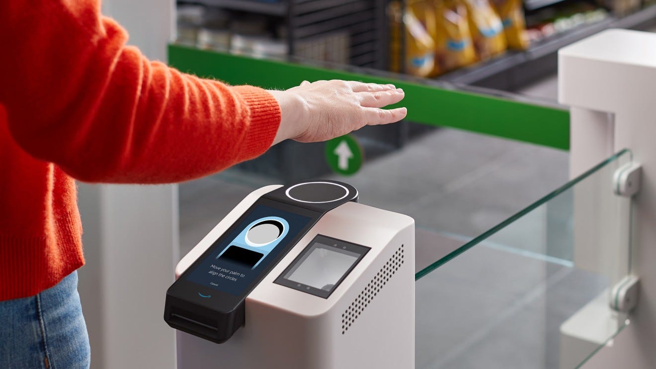 A person stands at a grocery entry gate with their hand suspended over a palm reading device. 