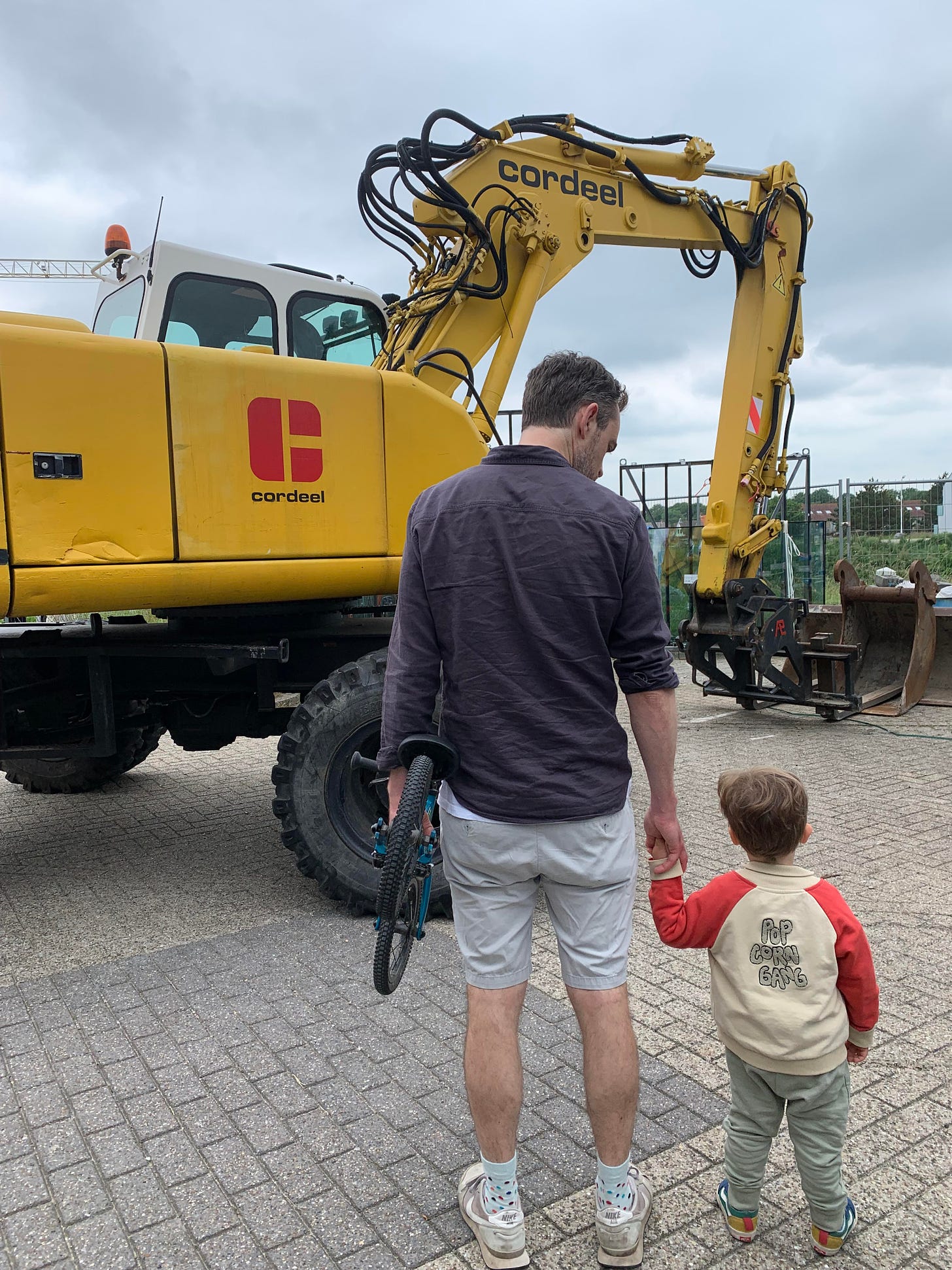 A photo of a boy and his son looking at a large yellow digger.