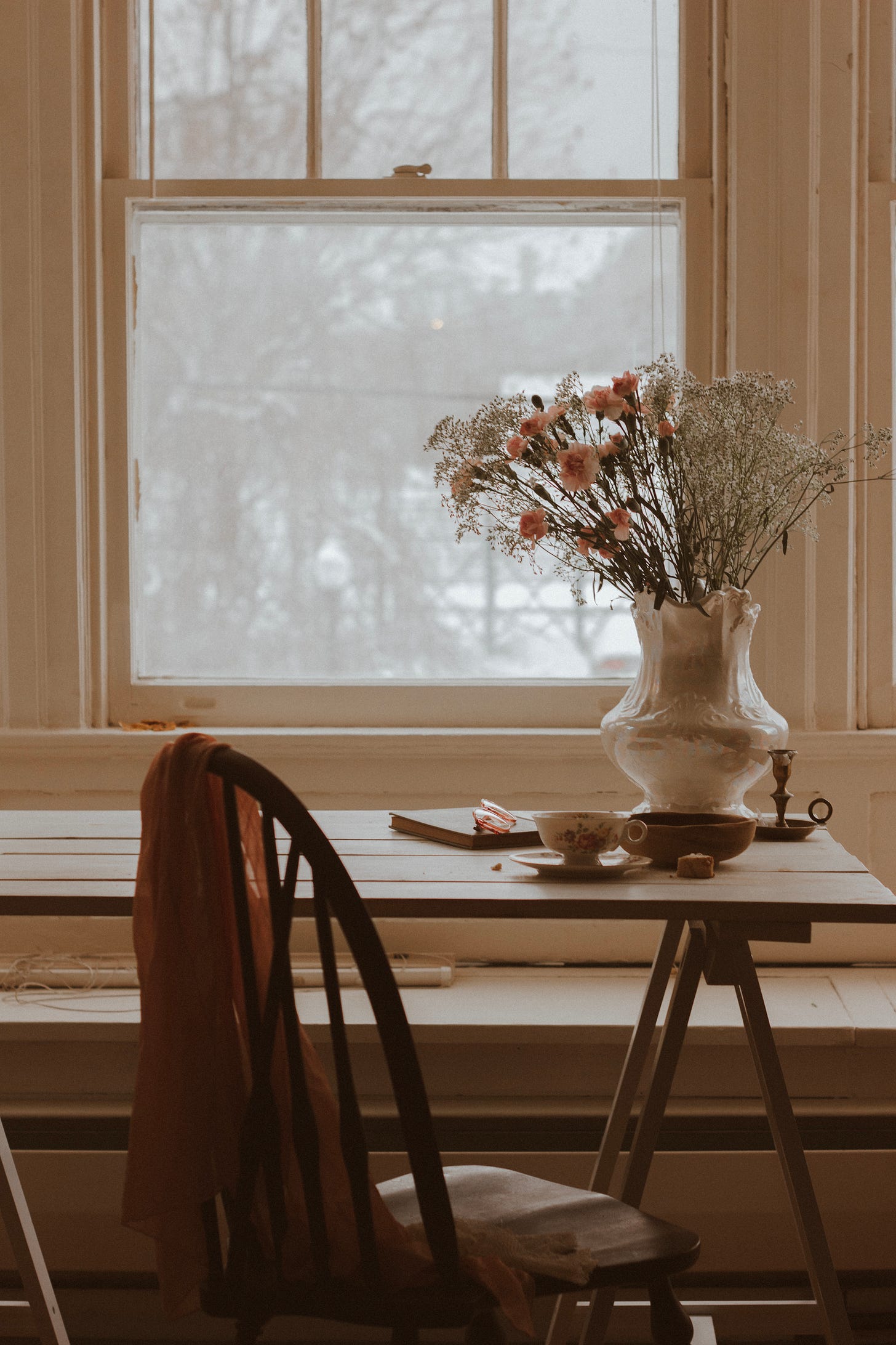 Table with flowers and a cup of tea looking out a wintery window
