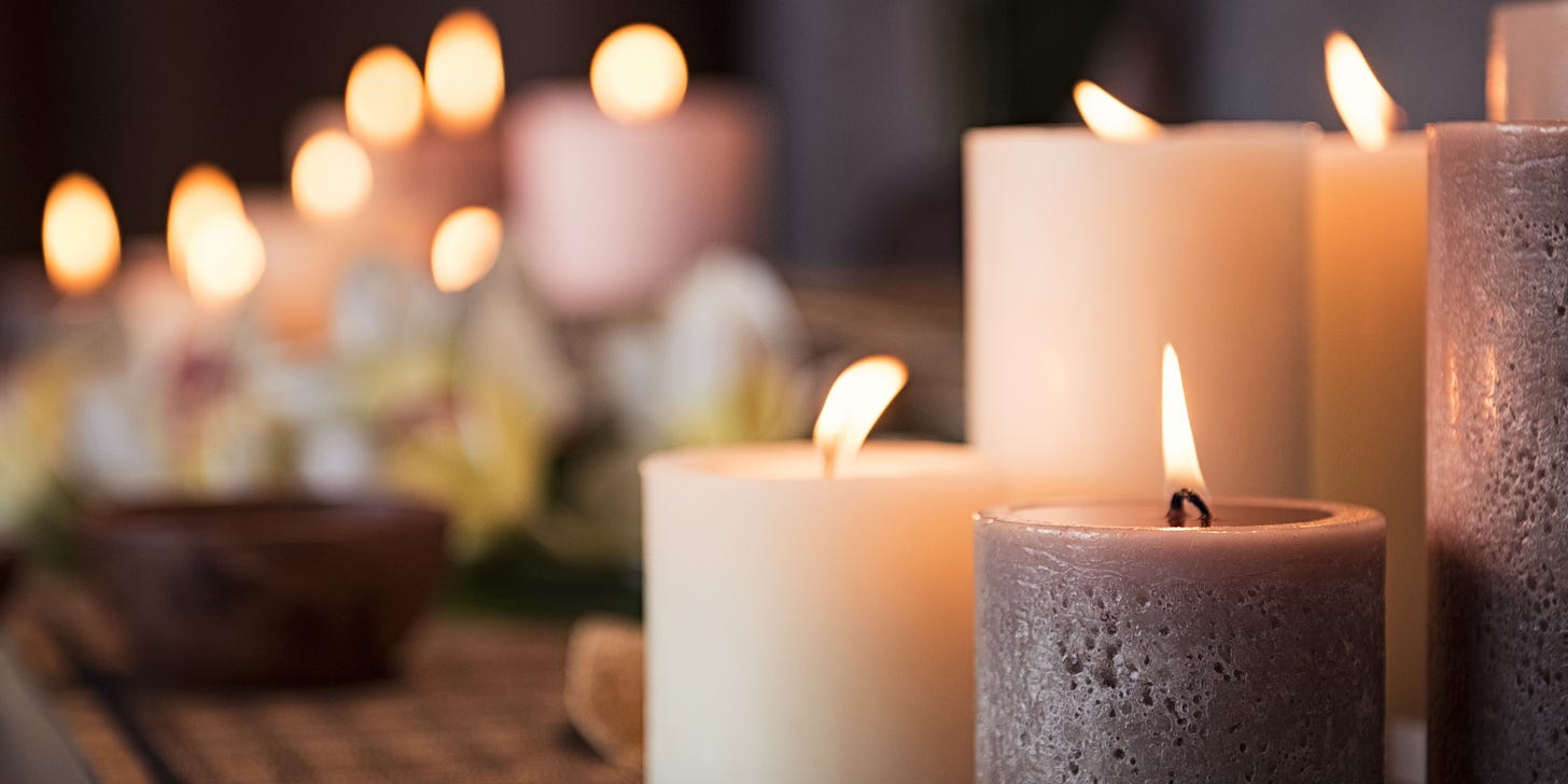 a cluster of lit white and gray candles in the foreground, with more lit candles blurred in the background
