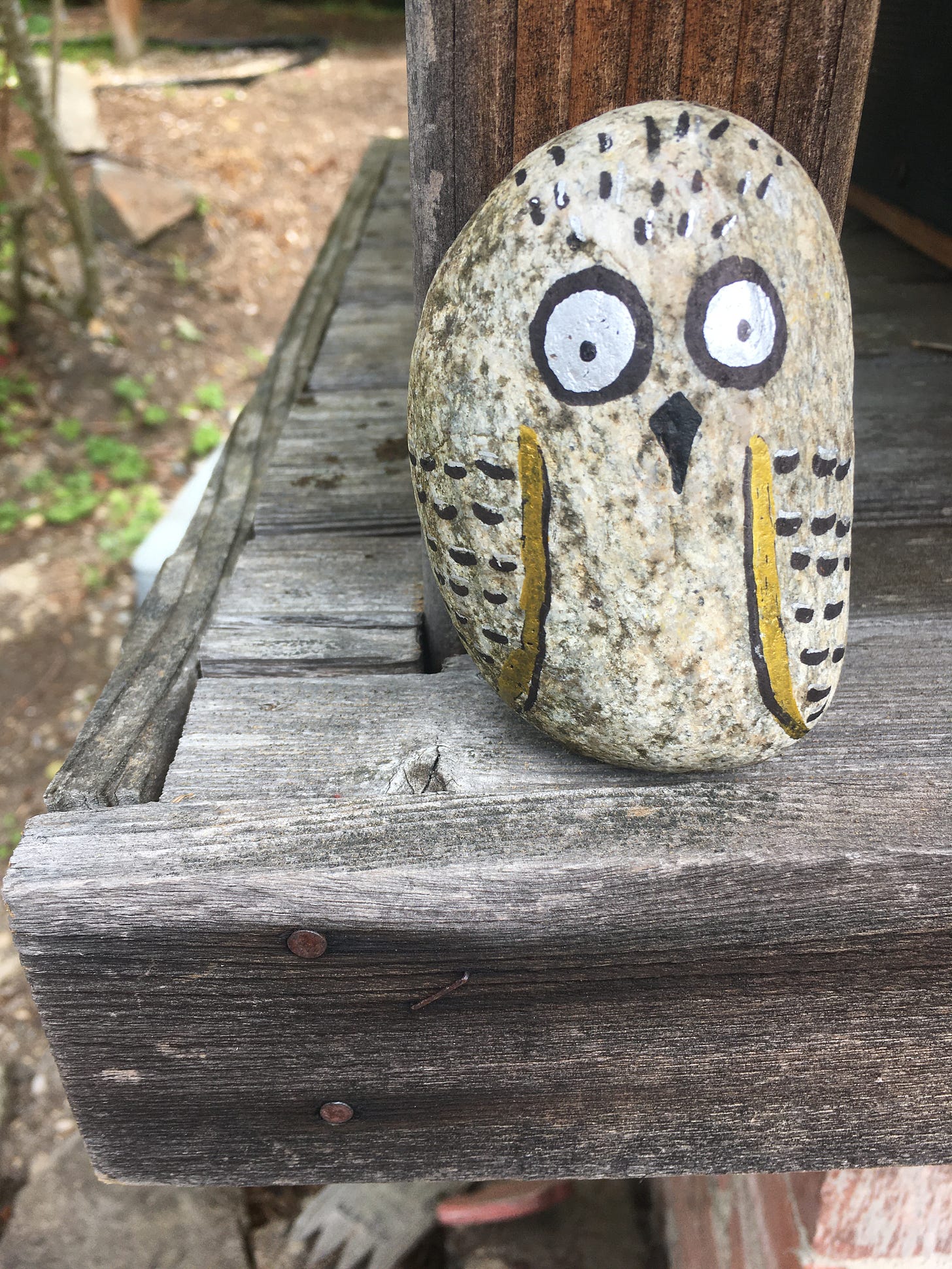 an oval-shapped stone painted into an owl with big round eyes. painted by a neighbor and set on the wooden home for mailboxes.
