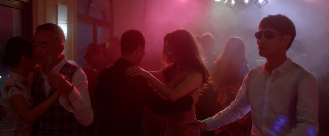 From the film "Touch": At a dance party, colored lights cover a group of tango couples, as a blind man tries to walk through.