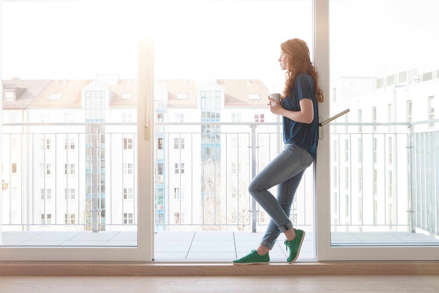 Woman in jeans with long red hair leaning against a sliding door on a balcony