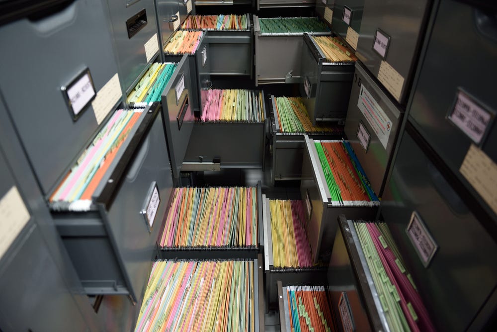 Two rows of file cabinets with some drawers open, displaying lots of paper files. It looks claustrophobic