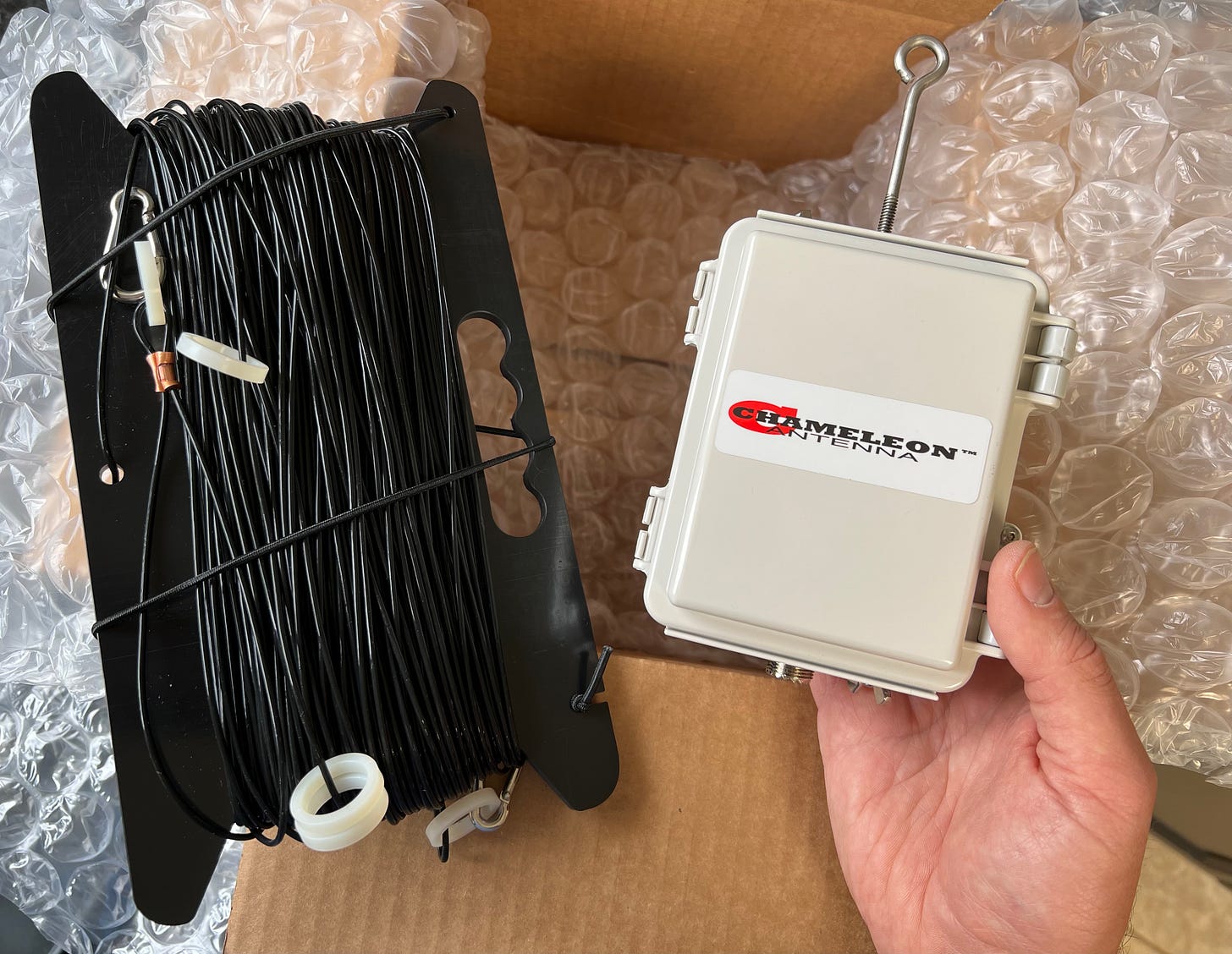 A spool of wire and box are shown above a cardboard box. All the parts of a Chameleon sky loop antenna