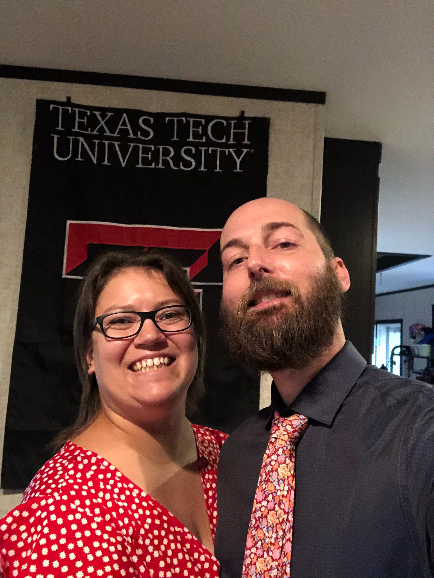 A white lady in a red polka-dotted dress and a bearded white dude in a blue shirt and pretty flower tie