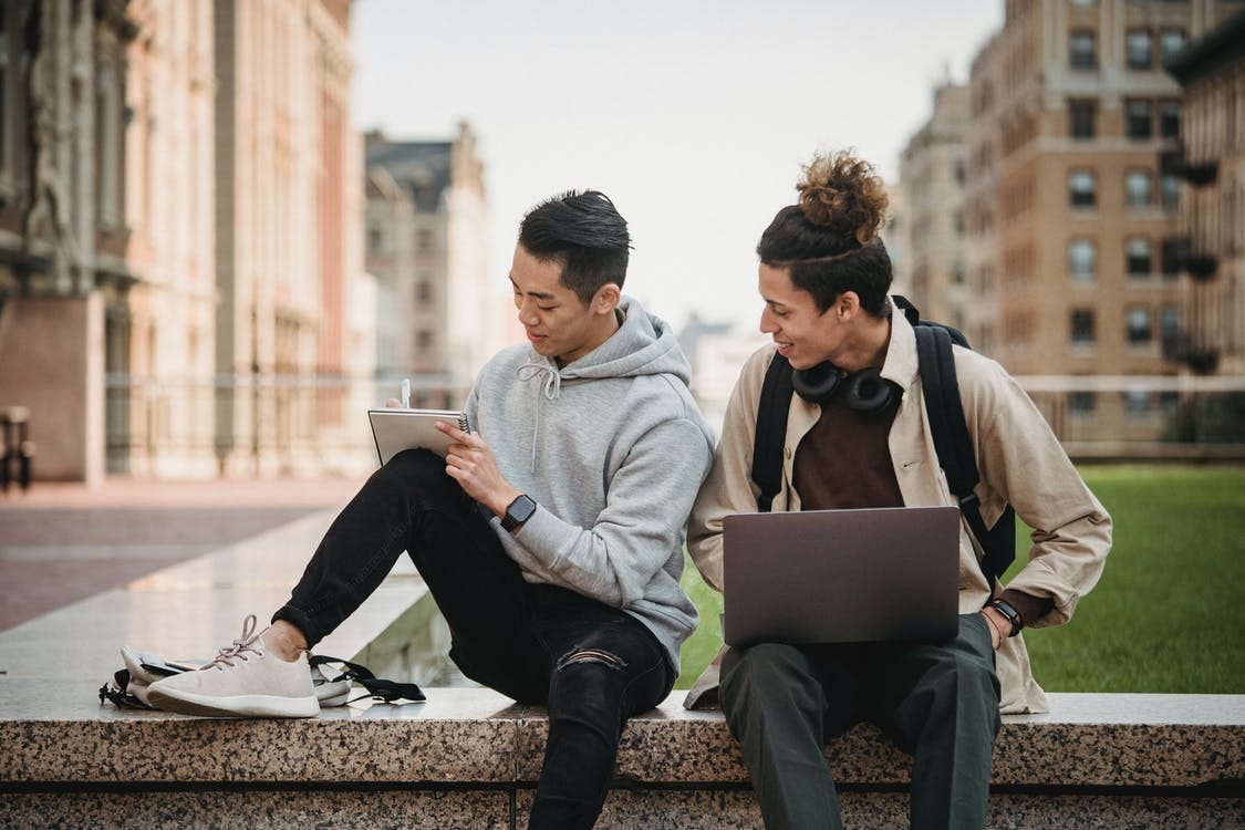 Man and Woman Sitting on Concrete Bench Using Laptop Computers