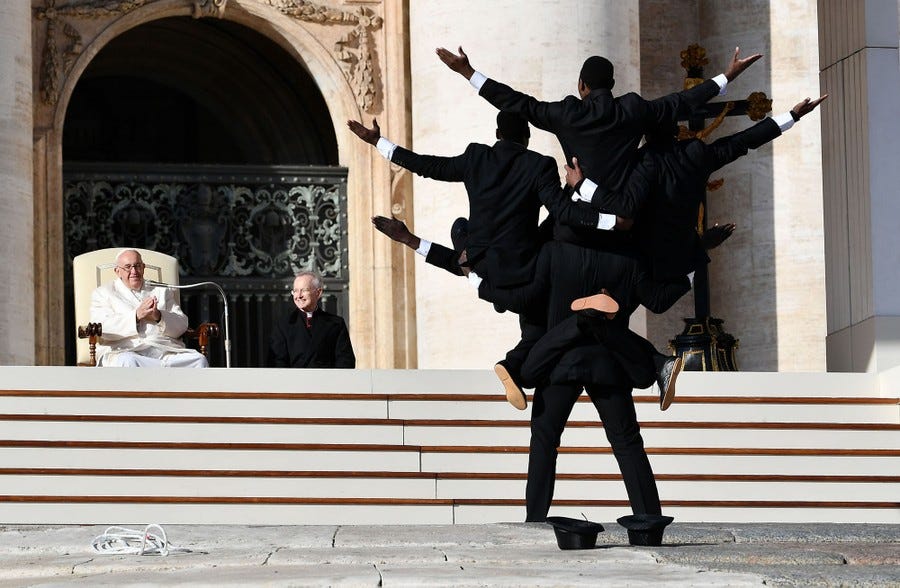 The pope watches a troupe of several performers, who pose while holding each other up.