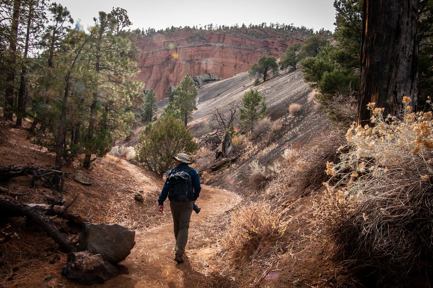 man with camera walks along trail into extinct volcano