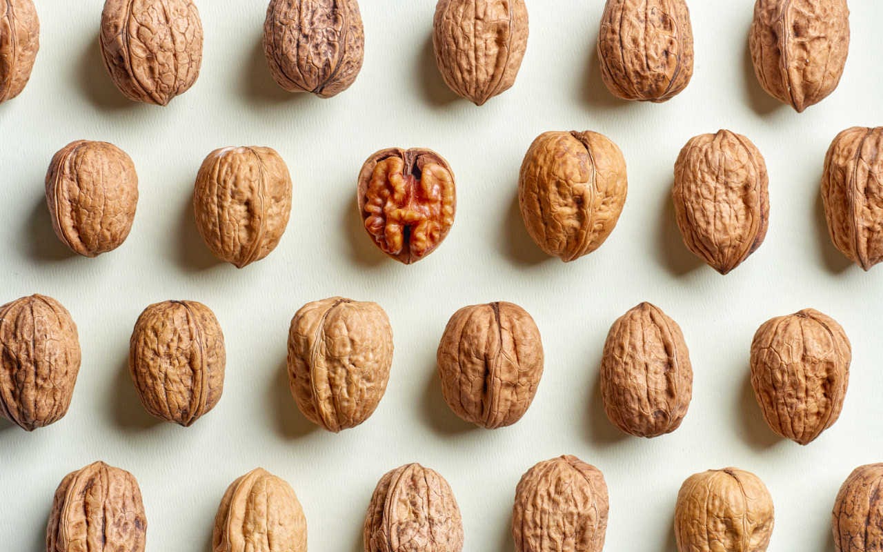 Rows of walnuts; all are in shells except for one in the middle that exposes the nut inside.