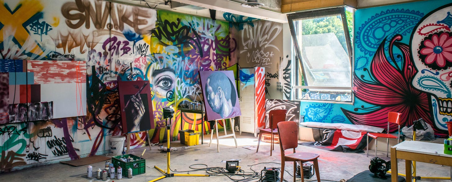 Artist's studio, with wall murals, art pieces on easels, and spray-paint cans on the floor.