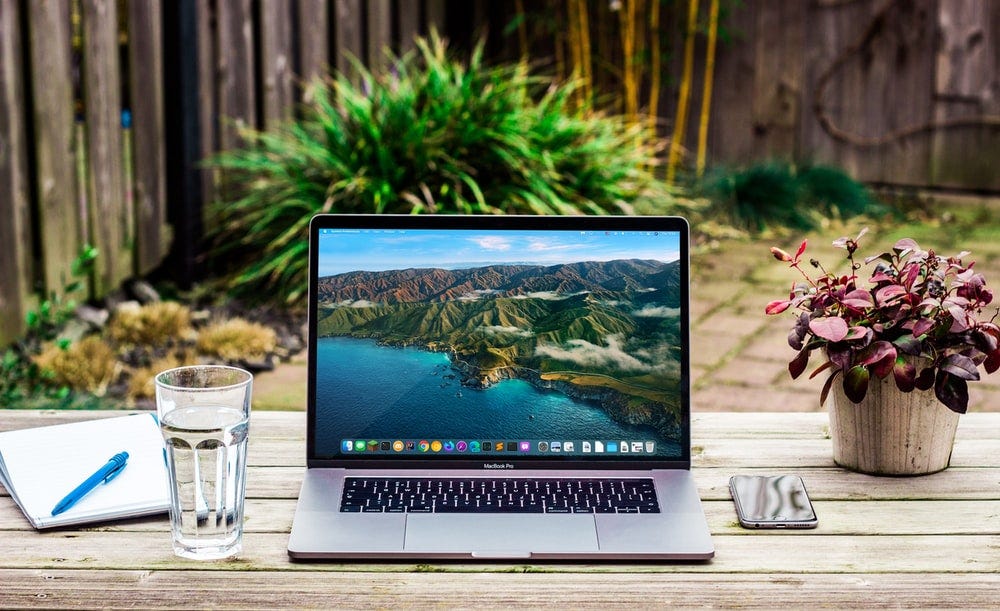 macbook pro beside clear drinking glass on brown wooden table macbook pro beside clear drinking glass on brown wooden table