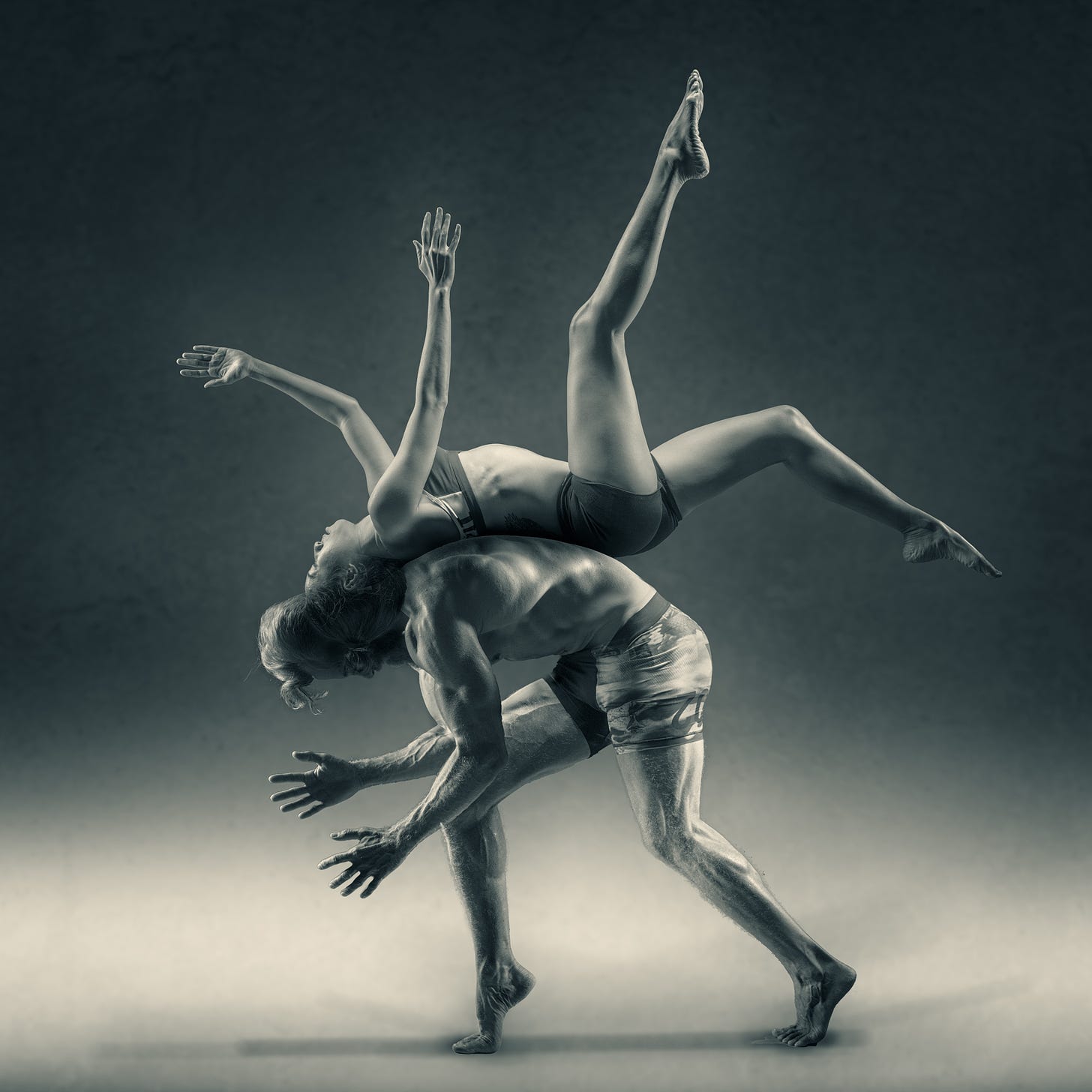 one person balancing on their back on top of the back of another person who is bent over. black and white photo