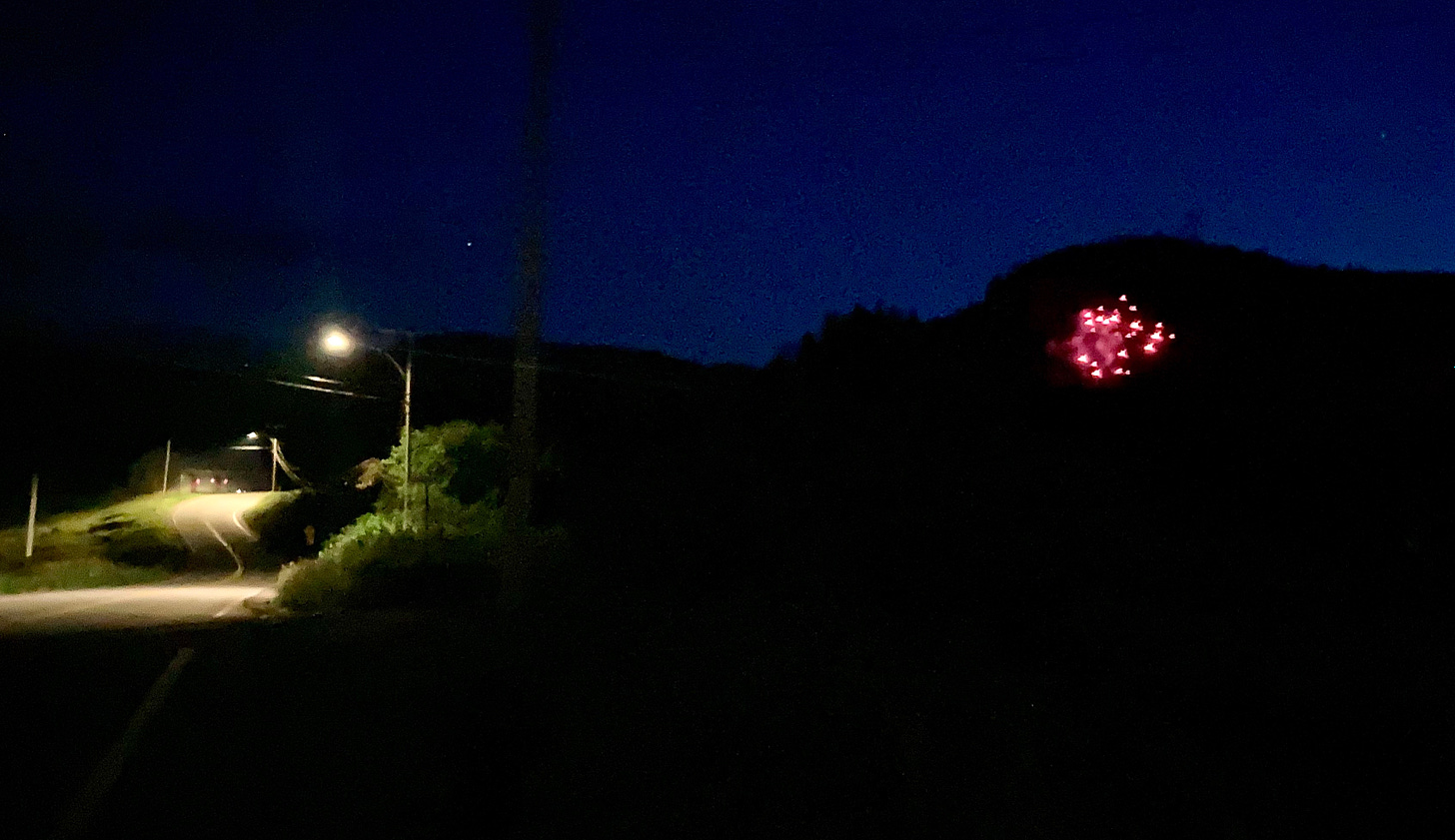 A nighttime picture with a curving road and a streetlamp on the left and a red firework on the right