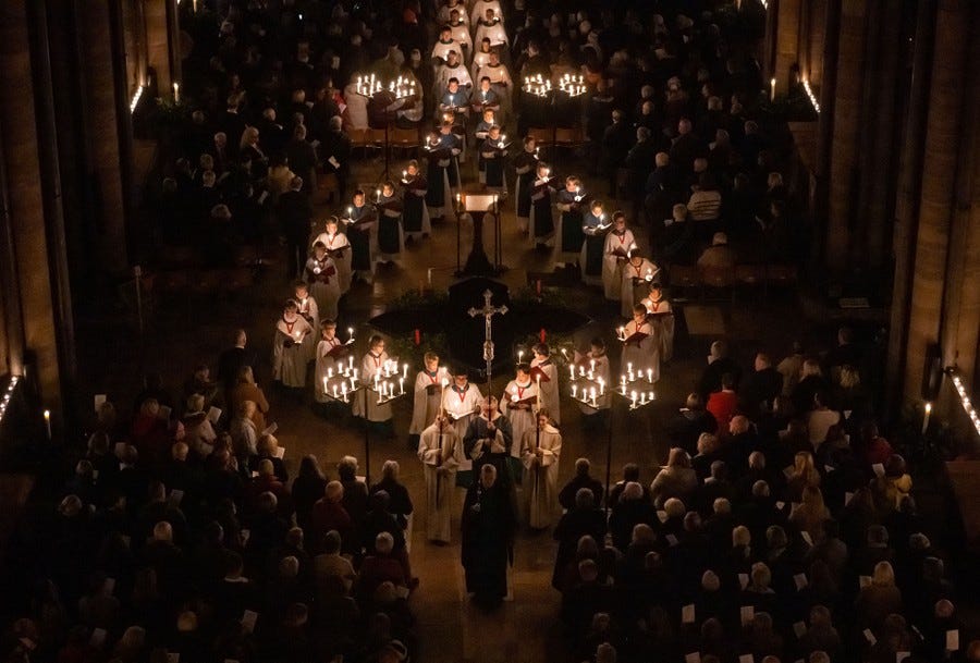 People fill the floor of a cathedral, as a procession walks through, carrying candles.