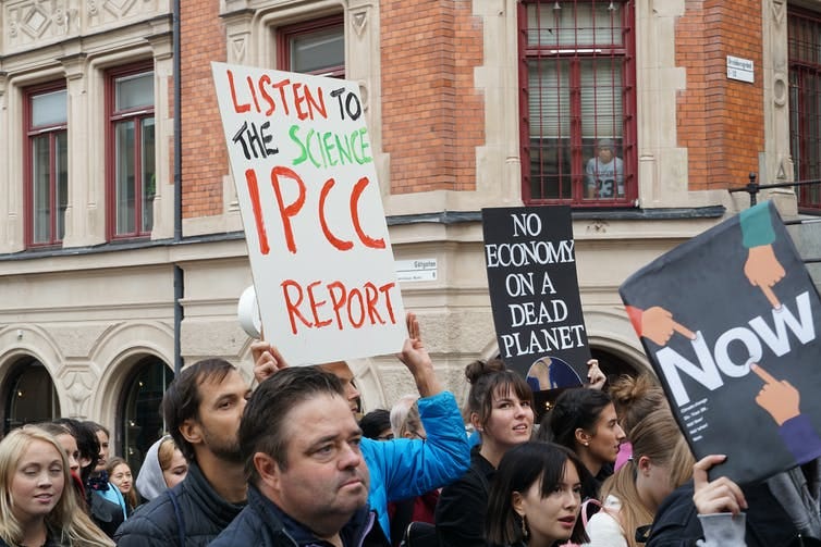 A protester holding a sign that says 'listen to the science, IPCC report'.