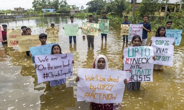 Nawfat Ibshar stands in floodwater and holds up poster saying 'We'll be dead by Cop27 #ActNow' with other protesters
