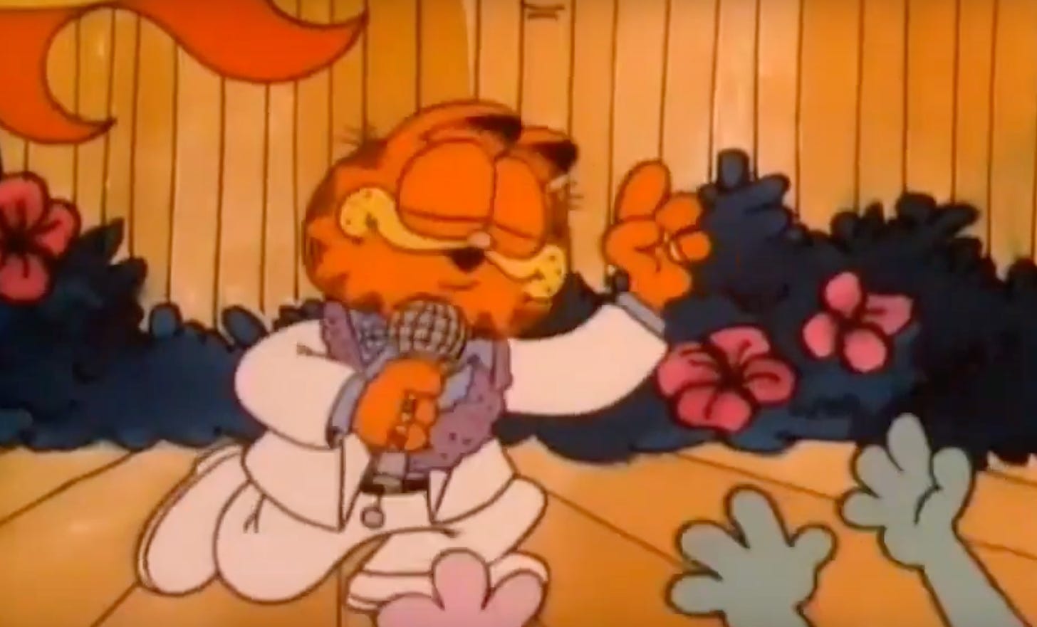 Garfield in a white suit sings into a microphone on a tropical stage with flowers as admiring fans reach out their paws toward him.