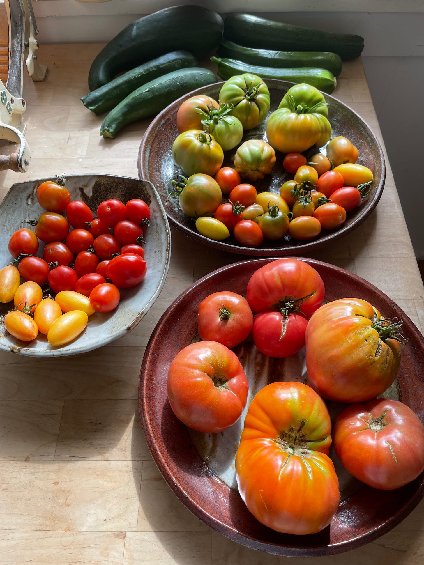 photograph of many tomatoes and zucchinis on a butcher block table