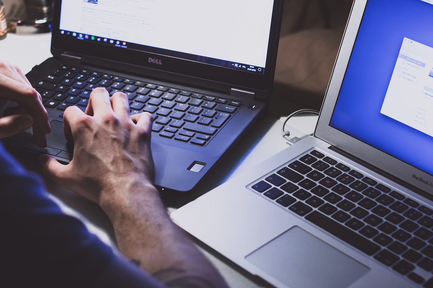Picture of a man typing on one laptop next to another. (Freestocks / Unsplash)