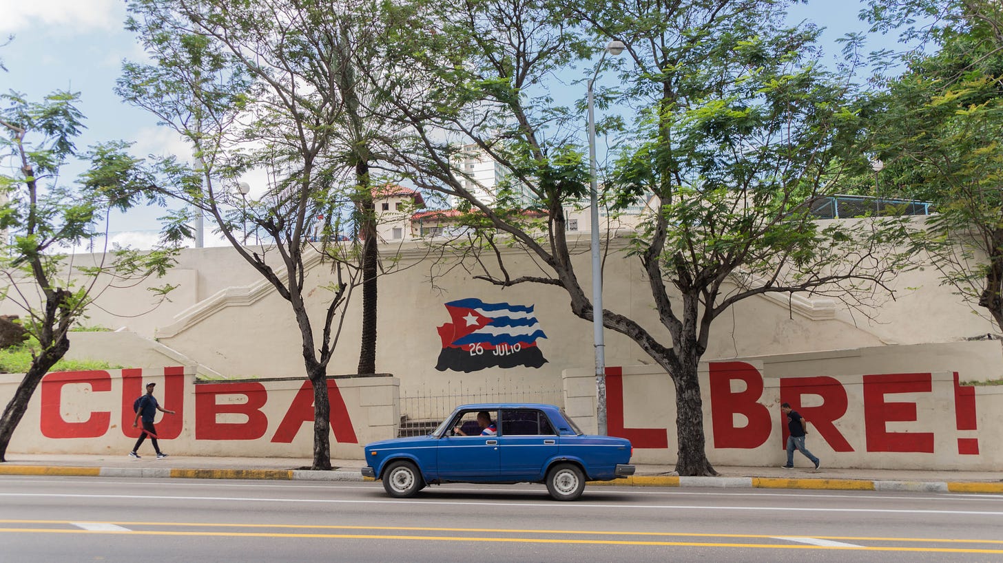 A blue car drives past a mural with trees scattered throughout.