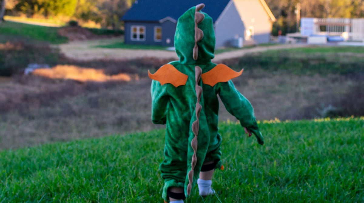 young boy wearing a dragon costume runs through grass towards home. Photo by Taylor Kopel on Unsplash