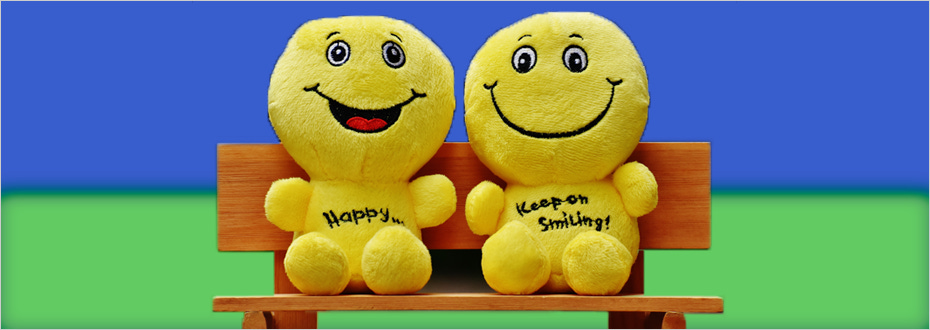 Two smiling yellow plush toy figures sit next to each other on a bench displaying the words ‘happy’ and ‘keep on smiling.’
