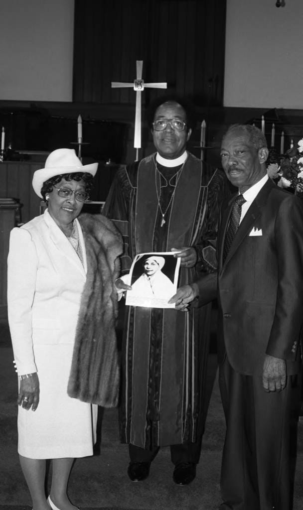 Rev. V. L. Brenson posing with a picture of Sarah Allen at Bryant Temple AME Church, Los Angeles, 1987