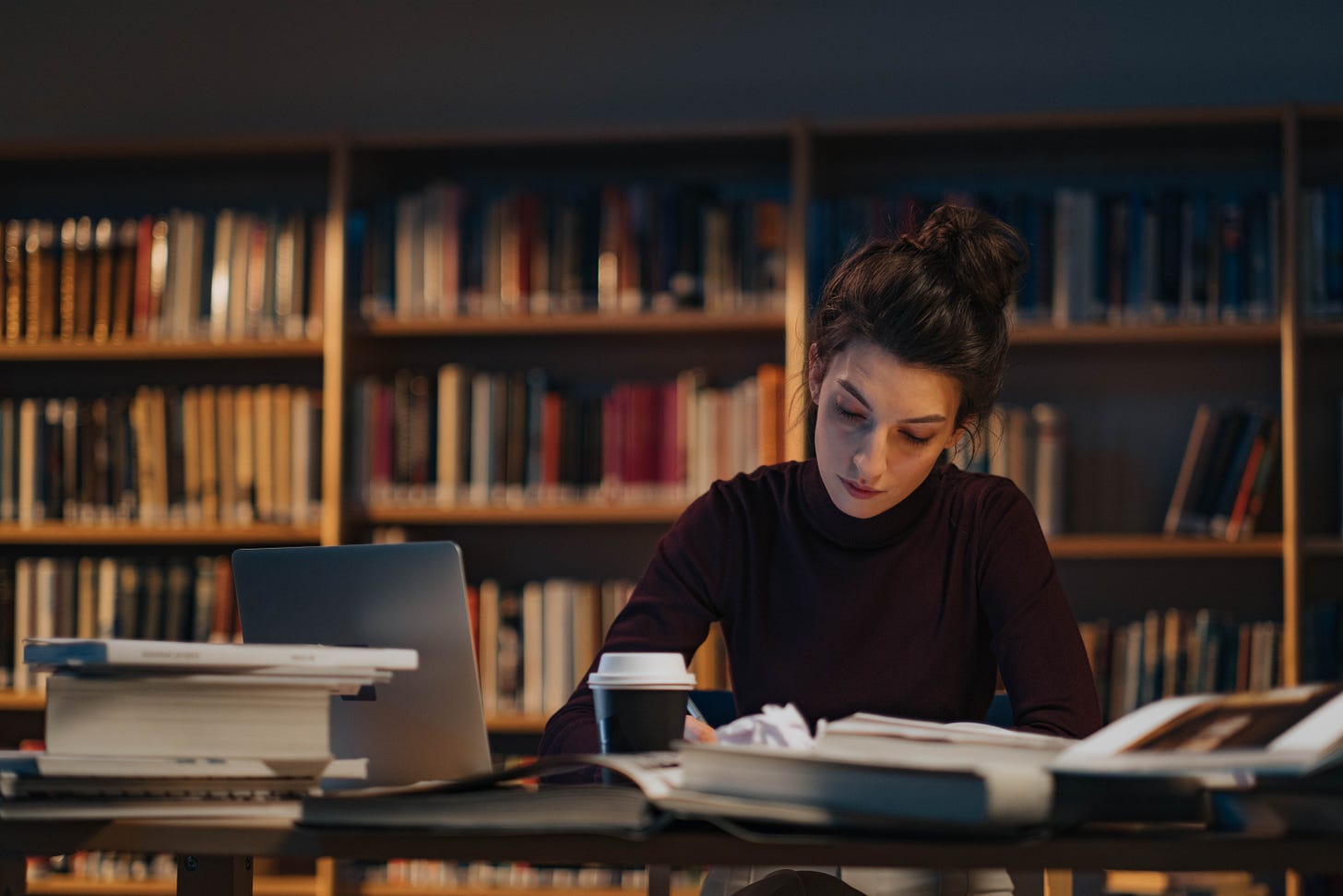 woman in library studying on desk with many books