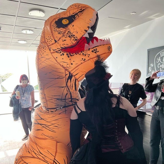 People looking at an 8 foot tall orange inflatable dinosaur at Fantasy Con 2022