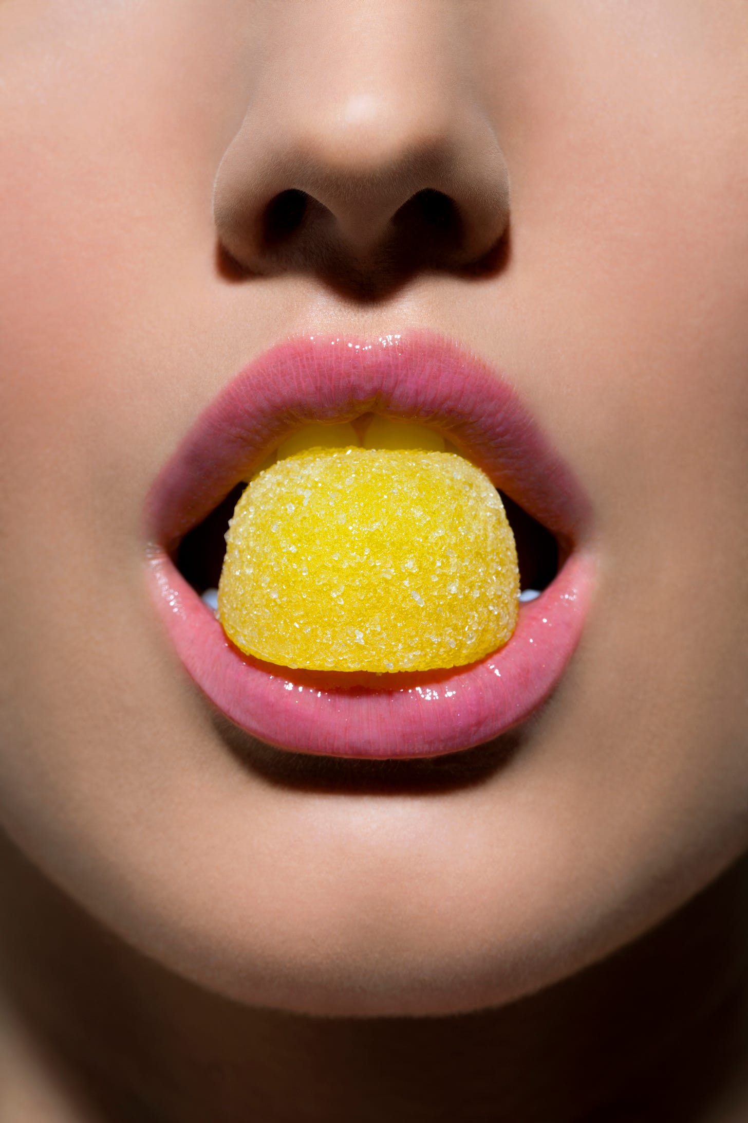 Woman with pale pink lipstick and a bright yellow candy between her teeth