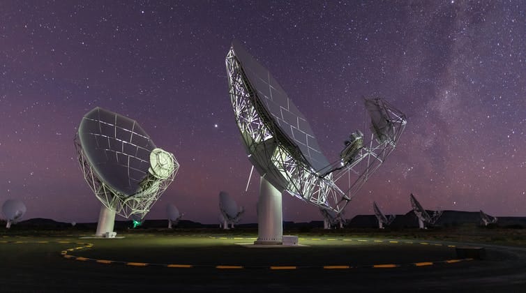 Two massive satellite dishes are pointed up towards the night sky