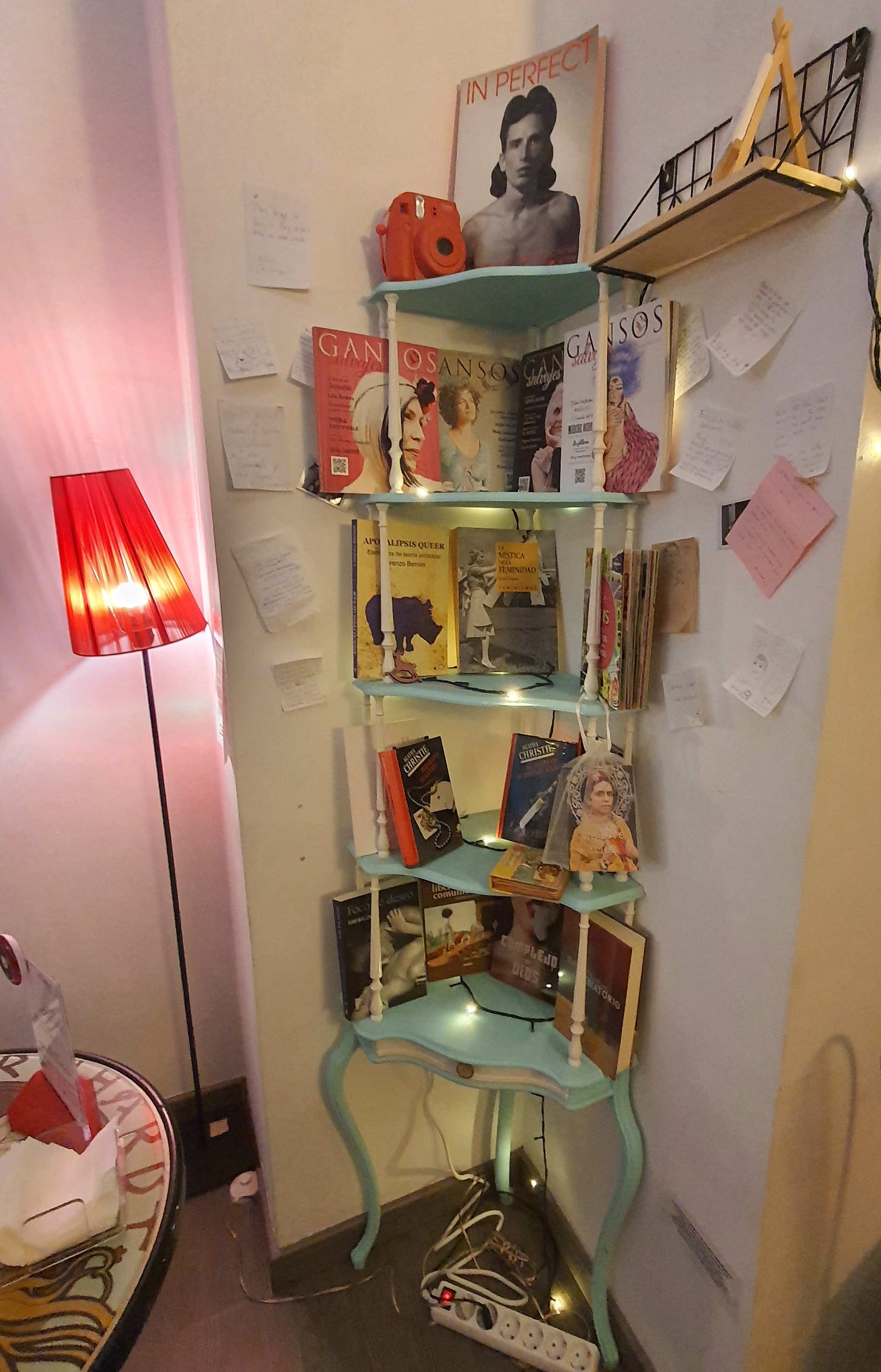 Feminist and queer literature on pale green corner stand, set off by pink walls and rosy lighting. 