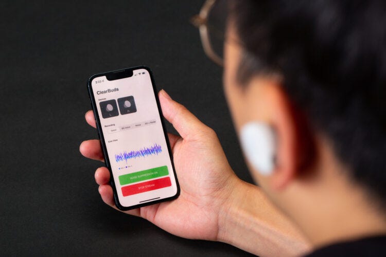 A person wearing earbuds and looking at their phone, which shows the ClearBuds app on it. App is showing details about the left and right earbuds and has the option to turn on noise suppression.