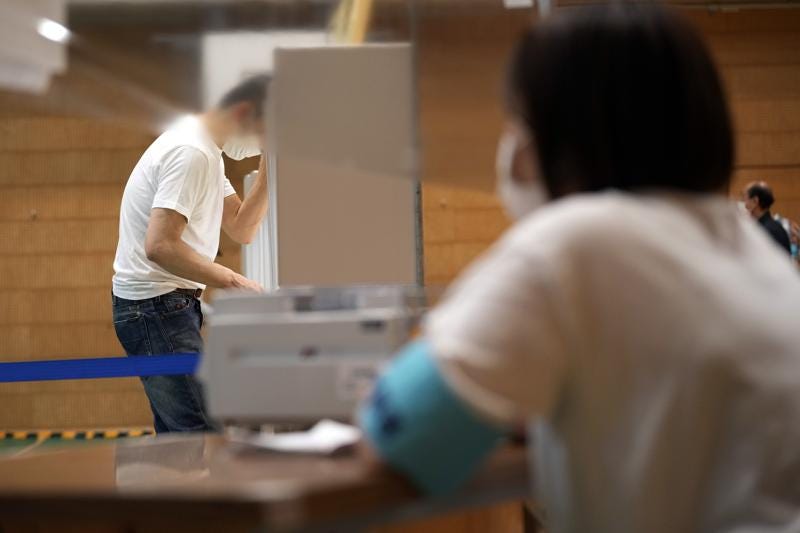 A staff member of a local election administration watches a voter preparing his ballot in the upper house elections at a polling station Sunday, July 10, 2022, in Tokyo. (AP Photo/Eugene Hoshiko)